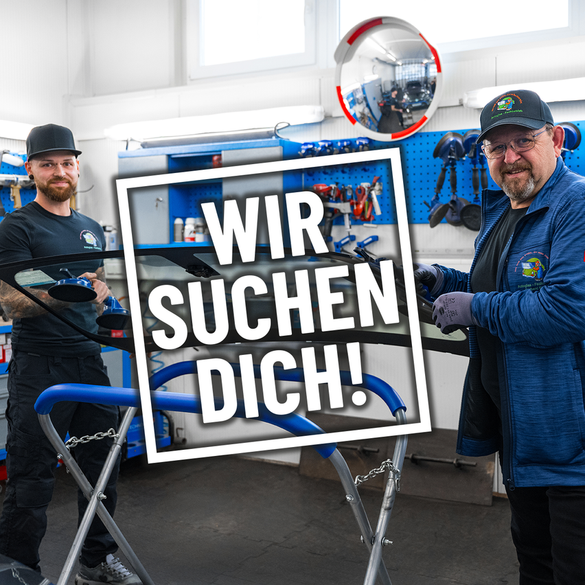 Zwei Männer stehen in einer Garage. Einer repariert die Windschutzscheibe eines Autos, während der andere lächelt in die Kamera. Ein Schild mit der Aufschrift 'Wir suchen Dich!' steht auf einem blauen Hintergrund.
