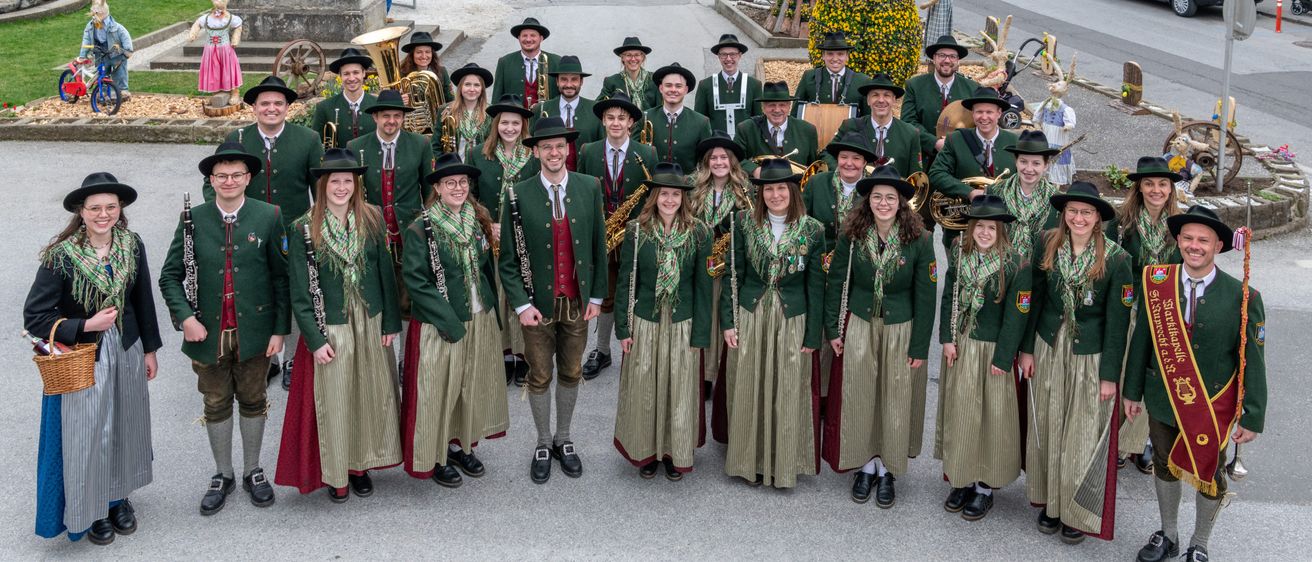 Eine Gruppe von Musikern in traditionellen Uniformen posiert für ein Foto im Freien. Sie halten Musikinstrumente wie Tuba und Klarinette.