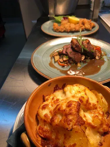 Zwei Teller mit Essen auf einem Tisch, einer mit einem Fleischgericht und der andere mit einem Käse-Kartoffelgericht.