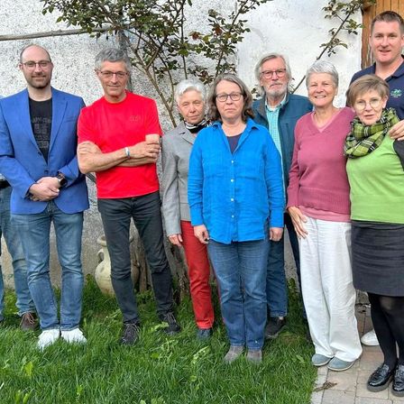 Eine Gruppe von Erwachsenen steht draußen in der Nähe einer Wand mit einem Baum. Sie alle lächeln und scheinen für ein Foto zu posieren.