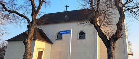 A church with a steeple, a street sign reading Pralat Zister Platz, and two leafless trees in front.