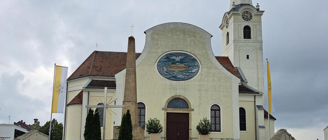 Eine Kirche mit einem braunen Dach und Turm steht mit Stufen, die zu ihrem Eingang führen. Eine Uhr befindet sich auf dem Turm.