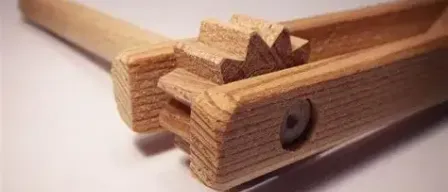 Ein hölzerne Spielzeug mit einem Griff und einem kleinen Holzblock, der an einem größeren Block mit einem Loch in der Mitte befestigt ist, auf einer weißen Oberfläche.