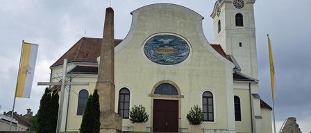 A church with a steeple, a cross, and a clock. There are two flags on either side of the church.