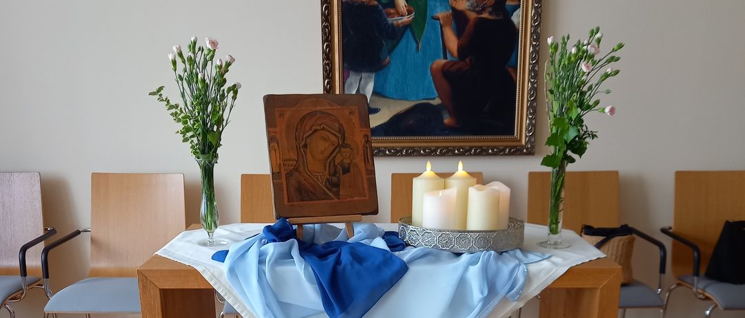 A wooden altar with a blue cloth, a statue of the Virgin Mary, and candles. A painting hangs on the wall behind it.