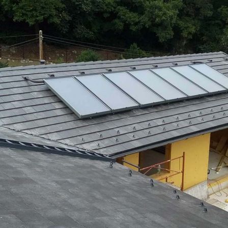 Eine Dachinstallation von Solarmodulen auf einem grauen Ziegeldach mit einem gelben Gebäude im Bau im Hintergrund.
