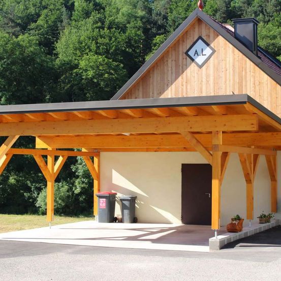 Ein Holzhaus mit einer Veranda und einem Schild, das AL steht. Es hat einen Mülleimer auf der linken Seite und zwei Topfpflanzen auf der rechten Seite.