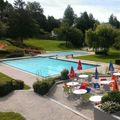 Ein Blick von oben auf ein Resort mit Schwimmbad, bunten Stühlen und Tischen mit Schirmen. Das Gebiet ist von üppigen grünen Bäumen und Pflanzen umgeben.