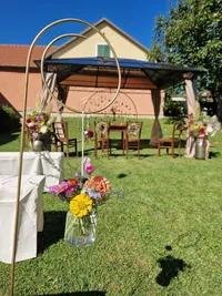 Eine Outdoor-Hochzeitsdekoration mit einem großen goldenen Ring, Blumenvasen und Holzstühlen unter einem Pavillon mit einer rosa Wand.