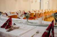 Ein festlich gedeckter Esstisch mit einem weißen Blumencenterpiece, einer roten Rose und einer Kerze. Weingläser und Besteck sind ordentlich auf einem weißen Tuch arrangiert.