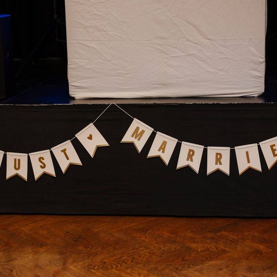 Ein Banner mit dem Wort Heirat hängt an einer Bühne. Es ist golden mit weißen Buchstaben. Ein Herz befindet sich auf der linken Seite des Banners.