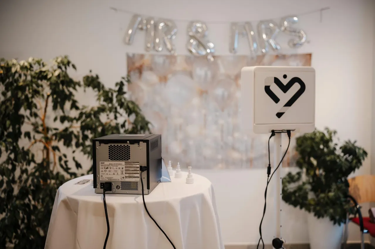 Ein Fotokabinen-Setup mit einem Computer und einer Fotokabinen-Maschine auf einem Tisch mit einer weißen Tischdecke.
