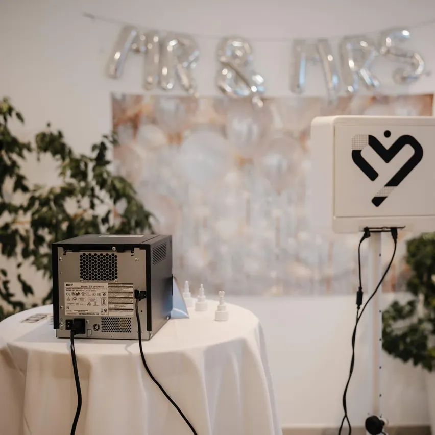 Ein Fotokabinen-Setup mit einem Computer und einer Fotokabinen-Maschine auf einem Tisch mit einer weißen Tischdecke.