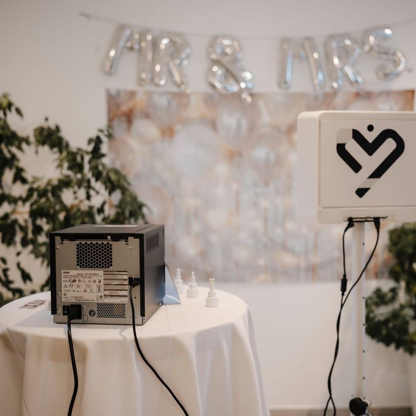 Ein Fotokabinen-Setup mit einem Computer und einer Fotokabinen-Maschine auf einem Tisch mit einer weißen Tischdecke.