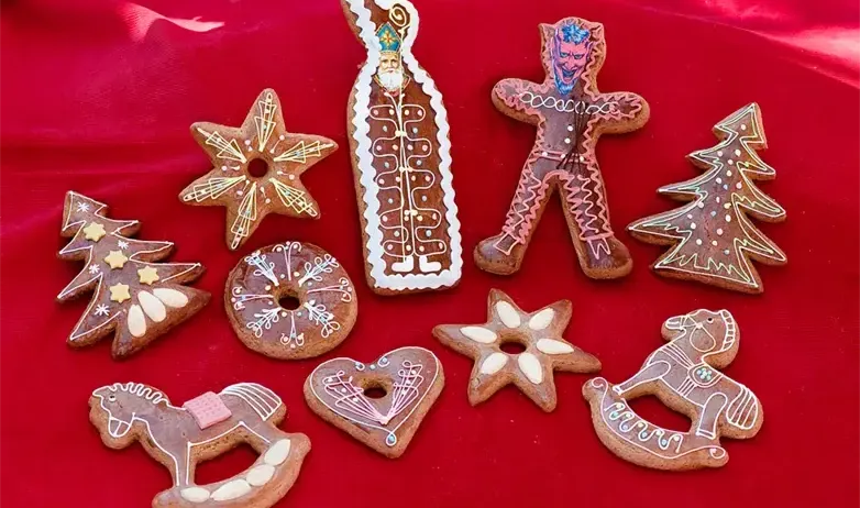 Verschiedene Lebkuchen-Plätzchen werden auf einem roten Tuch gezeigt. Sie umfassen Sterne, Bäume, ein Pferd, einen Mann und andere Formen.