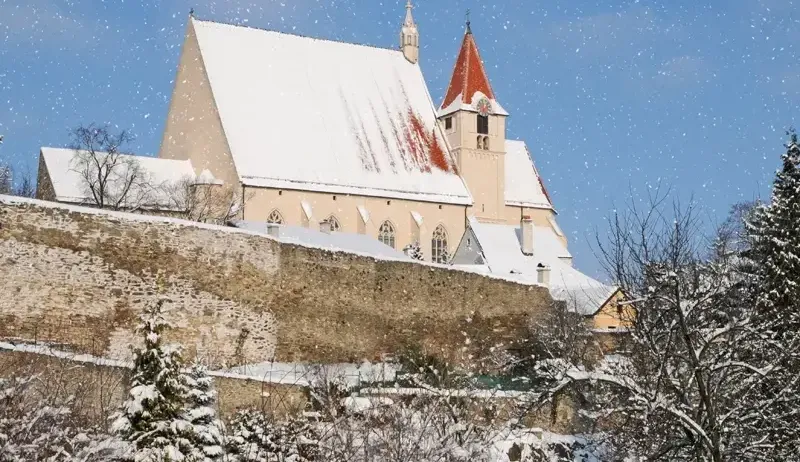Eine Kirche mit rotem Dach ist schneebedeckt, umgeben von schneebedeckten Bäumen und Büschen.