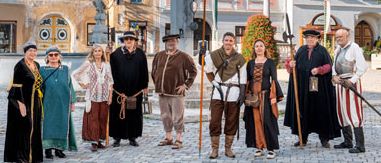 Eine Gruppe von Menschen in mittelalterlichen Kostümen steht vor einem Stadtplatz mit historischen Gebäuden.