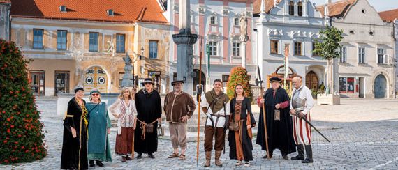 Eine Gruppe von Menschen in mittelalterlichen Kostümen posiert für ein Foto auf einem Stadtplatz mit historischen Gebäuden.