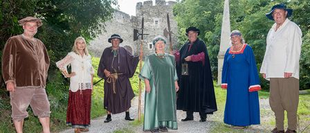 A group of people dressed in medieval attire, posing for a photo in front of an old castle.