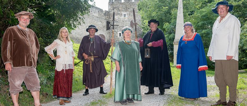 A group of people in historical costumes pose for a photo in front of a castle.