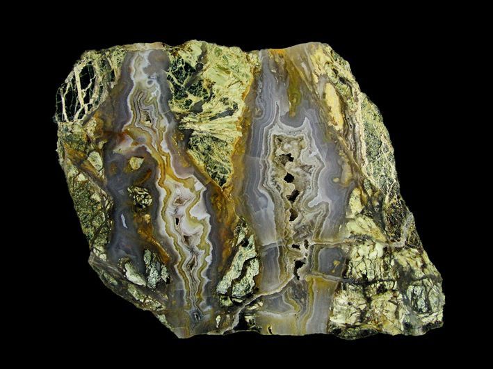 A close-up of a large, irregularly shaped rock with a mix of green, yellow, and gray colors. The rock has a rough texture and several holes.