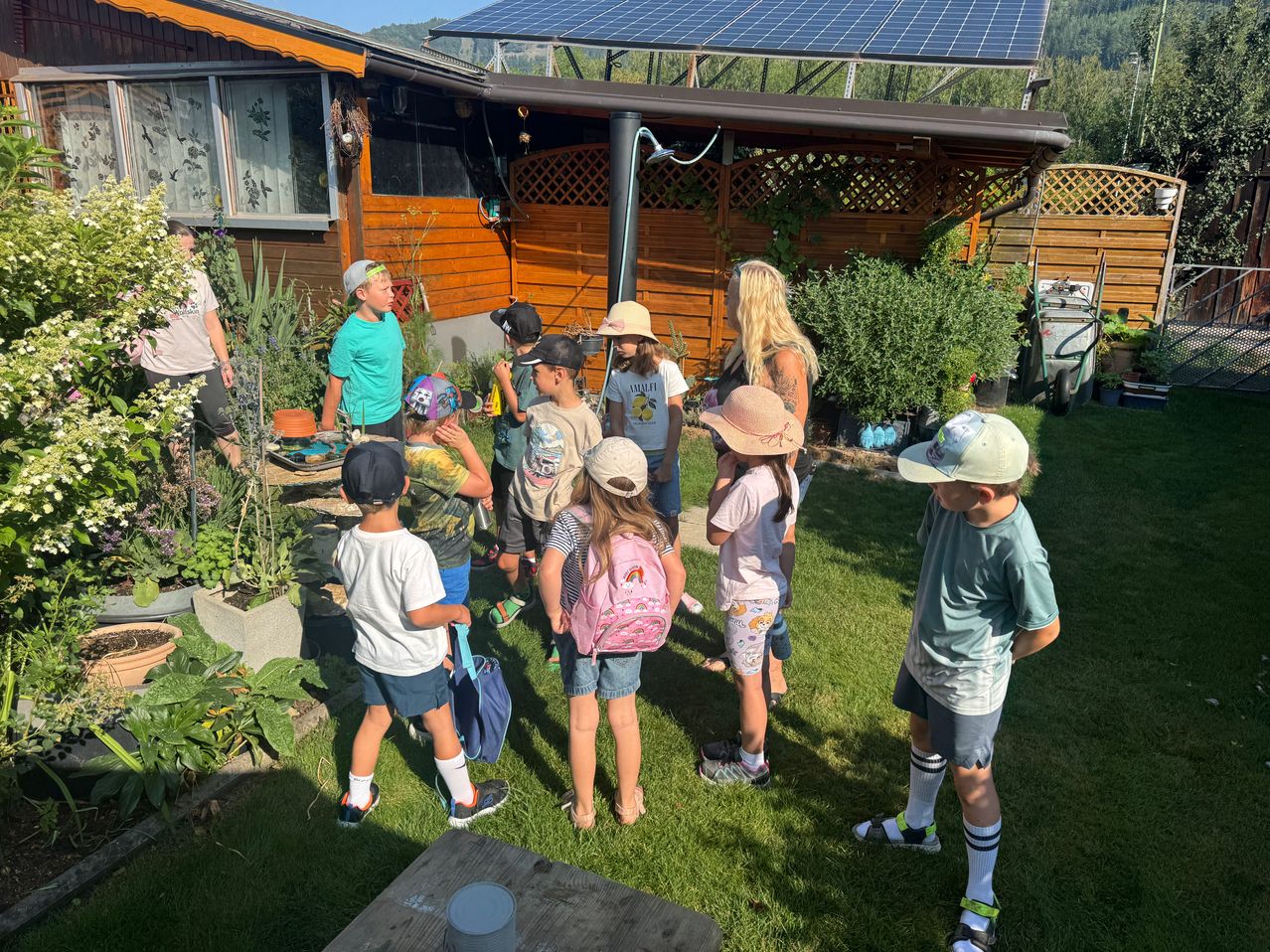 A group of children and adults are standing in a garden with solar panels on the roof of a house.