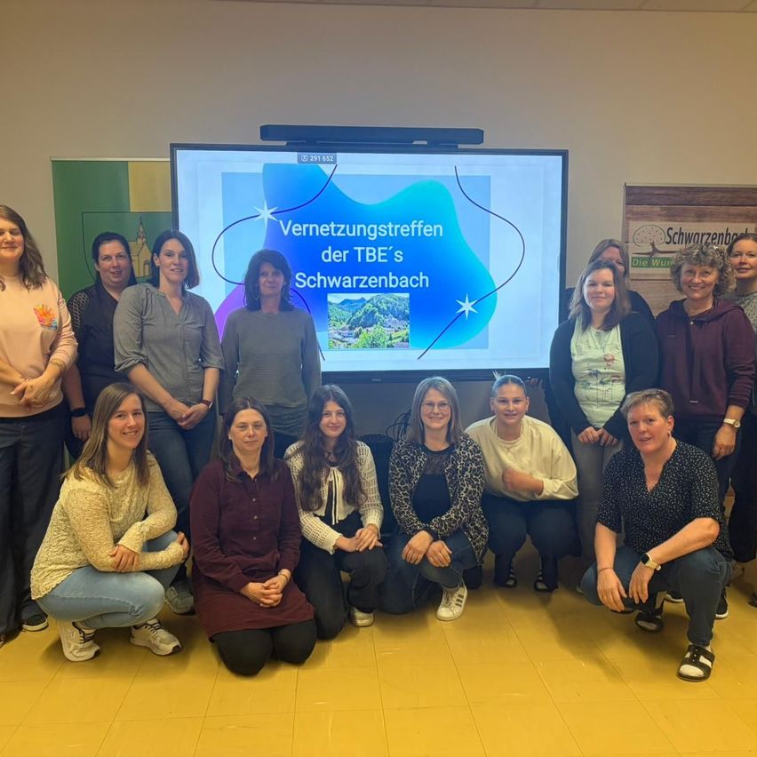 Eine Gruppe von Frauen posiert für ein Foto in einem Raum mit einem großen Bildschirm, auf dem 'Vernetzungstreffen der TBE's Schwarzenbach' steht.