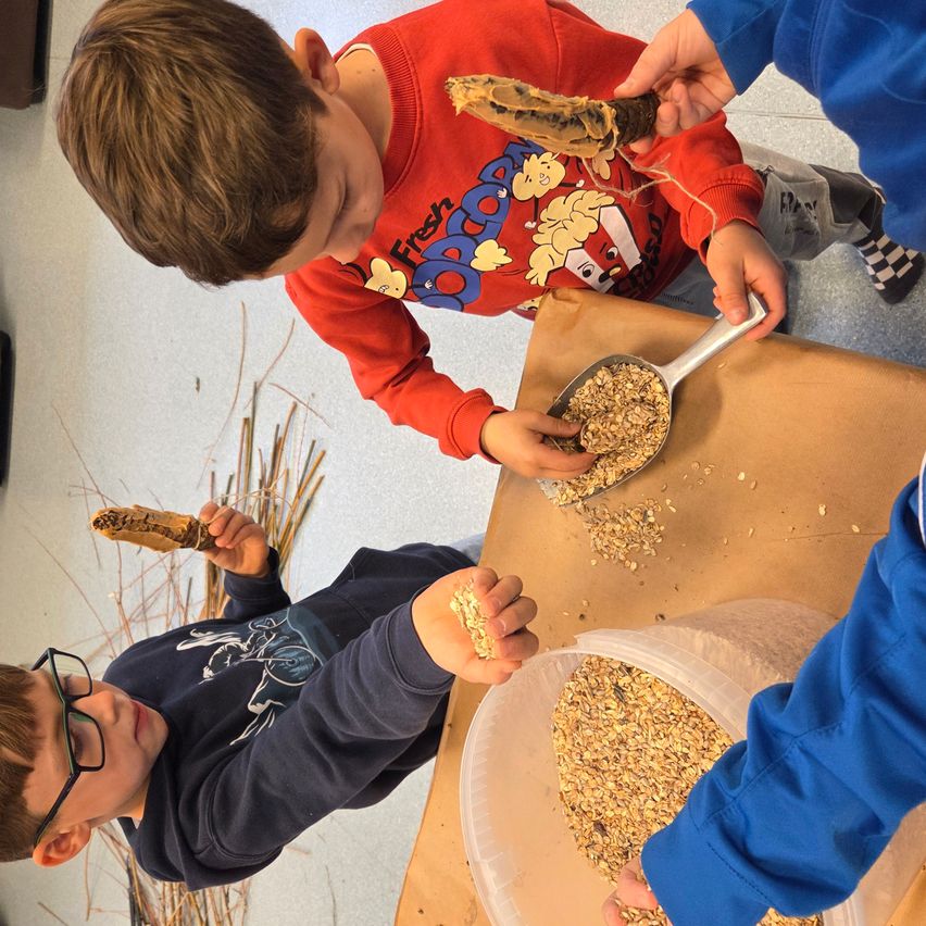 Drei Jungen sind mit einer Aktivität beschäftigt und halten Objekte, die Mais ähneln. Ein Junge hat einen Maiskolben mit einem Stück Fleisch, ein anderer hält ein Stück Mais und der dritte Junge hält einen Löffel mit Essen.