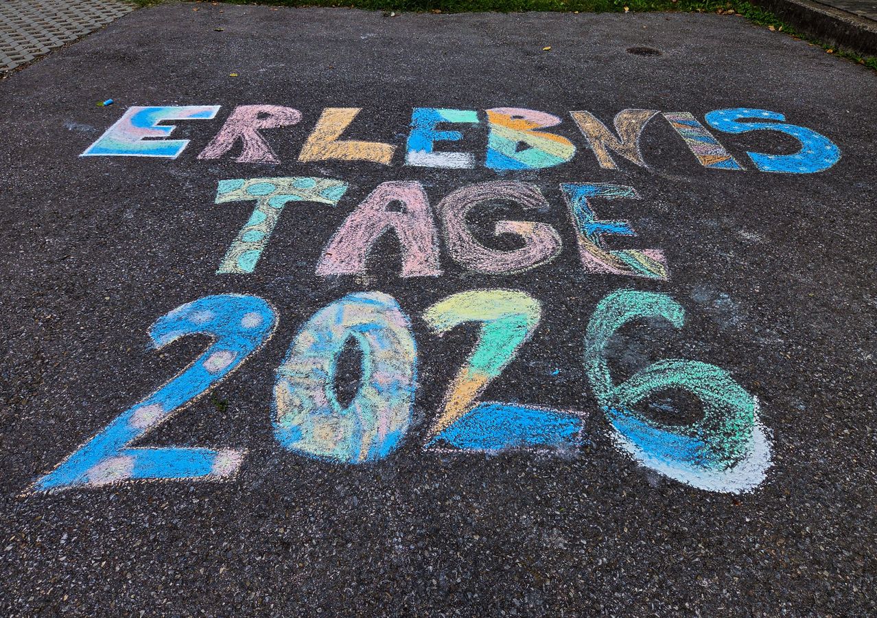 Kreidezeichnung auf dem Bürgersteig mit der Aufschrift 'ERLEBNIS TAGE 2026', Zahlen und Buchstaben in verschiedenen Farben.