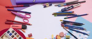 Ein Schreibtisch mit einem weißen Blatt Papier und verschiedenen Schulutensilien wie Bleistiften, Kugelschreibern, Scheren und einem Stiftetui ist darauf verstreut.