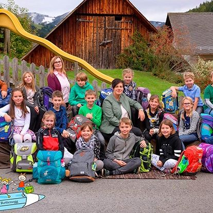 Eine Gruppe von Schülern und einer Lehrerin posiert für ein Foto vor einem Haus, einem Holzhaus und einer Rutsche.