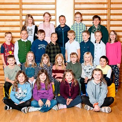 Eine Gruppe von Kindern in einem Fitnessstudio. Die Kinder lächeln und posieren für ein Gruppenfoto. Sie stehen und sitzen auf einem Holzboden.