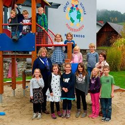 Eine Gruppe von Kindern und Erwachsenen posiert für ein Foto im Spielplatz mit einer blauen Rutsche und einem Logo an der Wand.