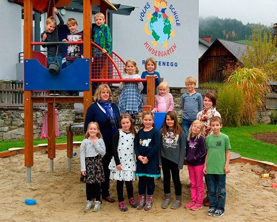 Eine Gruppe von Kindern und Erwachsenen posiert für ein Foto im Spielplatz mit einer blauen Rutsche und einem Logo an der Wand.