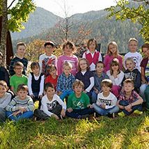 Eine Gruppe von Kindern und Erwachsenen posiert für ein Foto auf einem Rasenfeld, mit Bergen im Hintergrund.