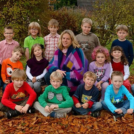 Eine Gruppe von Schülern und eine Lehrerin posieren für ein Foto in einem Park mit gefallenen Blättern.