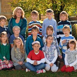 Eine Gruppe von Kindern und einer Frau sitzen auf dem Rasen vor einem Gebäude.