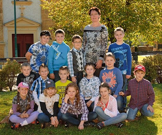 Eine Gruppe von Kindern und eine Frau stehen vor einem Kirchengebäude mit Herbstlaub.