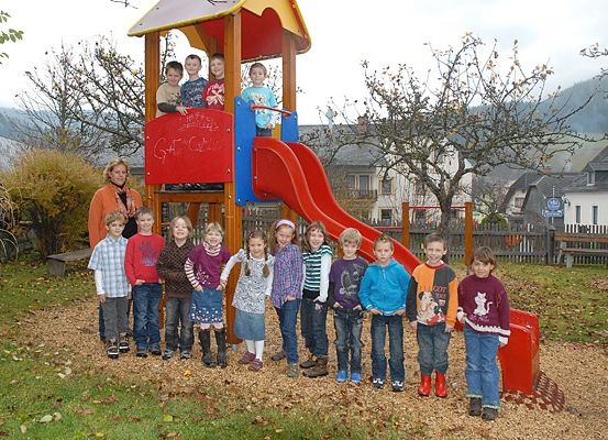Eine Gruppe von Kindern und zwei Erwachsenen posiert vor einer bunten Spielstruktur mit einer roten Rutsche.