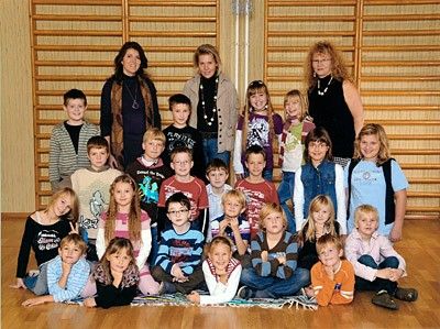 Eine Gruppe von Kindern und drei Erwachsenen posiert für ein Foto in einem Raum mit Holzwänden und -boden.