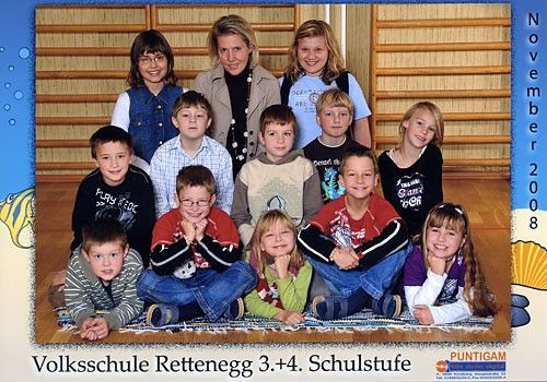 Eine Gruppenaufnahme von Schülern und einer Lehrerin an der Volksschule Rettenegg. Die Schüler sitzen auf dem Boden, während die Lehrerin hinter ihnen steht. Das Bild ist vom November 2008.
