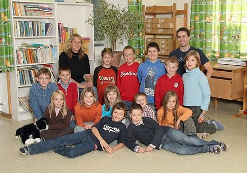 Ein Klassenfoto einer Gruppe von Kindern, zwei Lehrern und einer Pflanze. Die Kinder sitzen auf dem Boden, während die Lehrer hinter ihnen stehen.