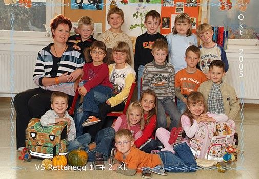 Eine Gruppenaufnahme einer Kindergartenklasse mit ihrer Lehrerin im Jahr 2005, sitzend und stehend in Reihen, in Freizeitkleidung, mit einem Halloween-Kürbis und Schulranzen im Hintergrund.