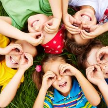 Eine Gruppe von Kindern liegt auf dem Gras, lächelt und macht Handgesten mit ihren Fingern.