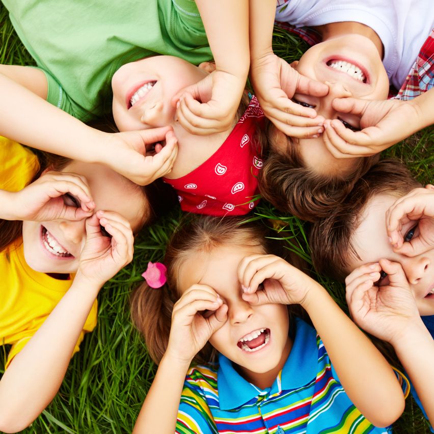 Eine Gruppe von Kindern liegt auf dem Gras, lächelt und macht Handgesten mit ihren Fingern.