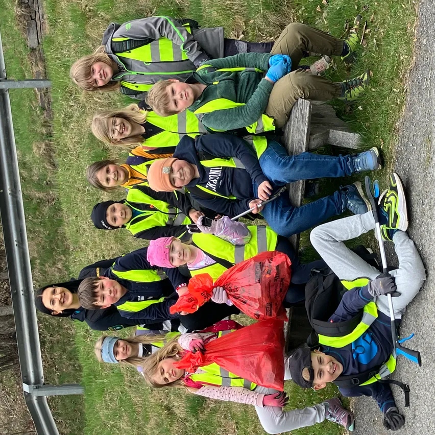 Eine Gruppe von Menschen in Warnwesten sitzt und steht auf dem Rasen. Sie haben Müllsäcke und Stöcke. Sie lächeln und posieren für ein Foto.