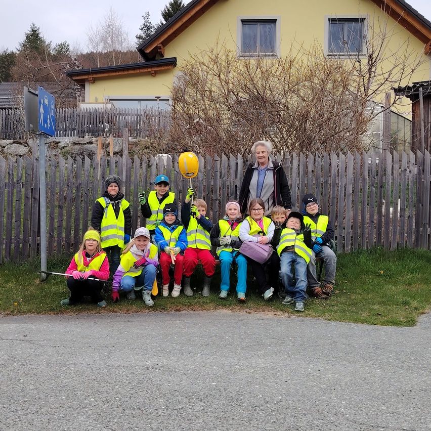 Gruppe von Kindern und Erwachsenen in Warnwesten posiert für ein Foto vor einem Haus und Zaun.