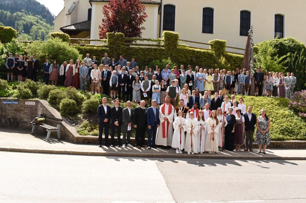 Eine große Gruppe von formell gekleideten Menschen posiert für ein Foto vor einer Kirche. Einige halten Kerzen.