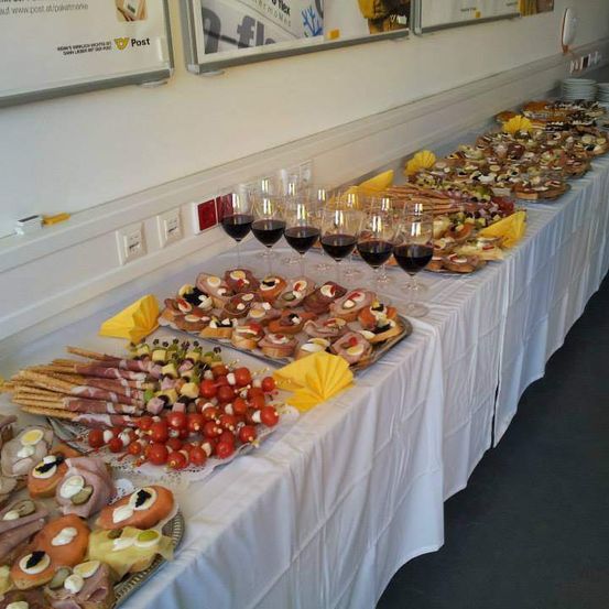 Ein langer Tisch mit einer Vielzahl von Speisen, Weingläsern und Tellern. Es gibt Fleisch, Gemüse und Gebäck.