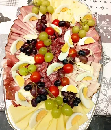 Ein großer Teller zeigt eine Auswahl an Schinken, hart gekochten Eiern, Käse, Tomaten und Trauben.